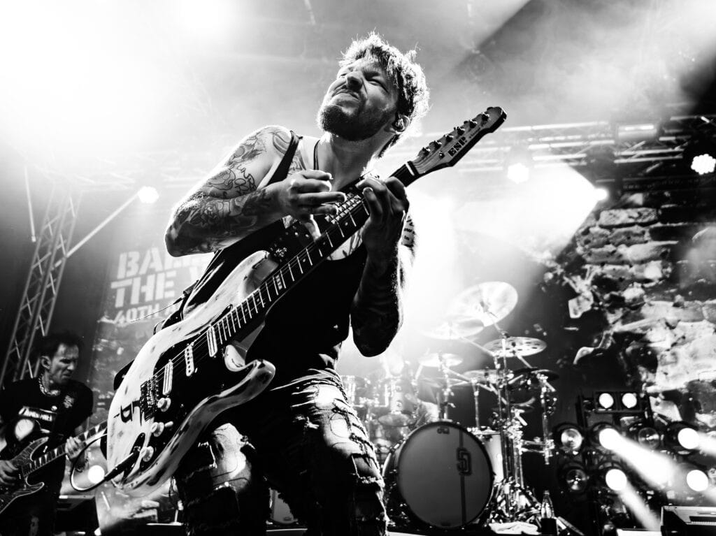 Dee Dammers playing guitar on stage during a live concert.